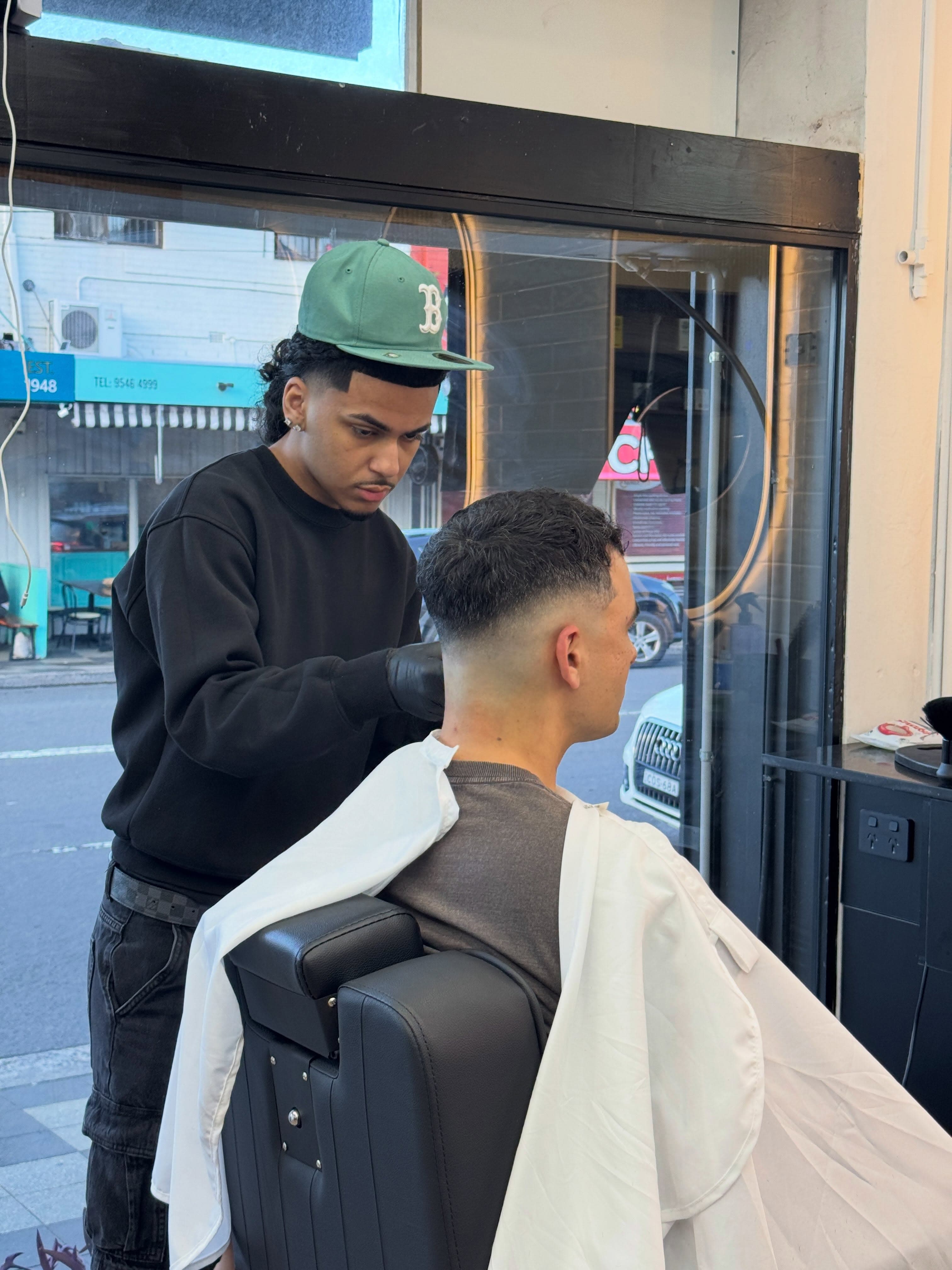 Barber cutting a client's hair by the shopfront window